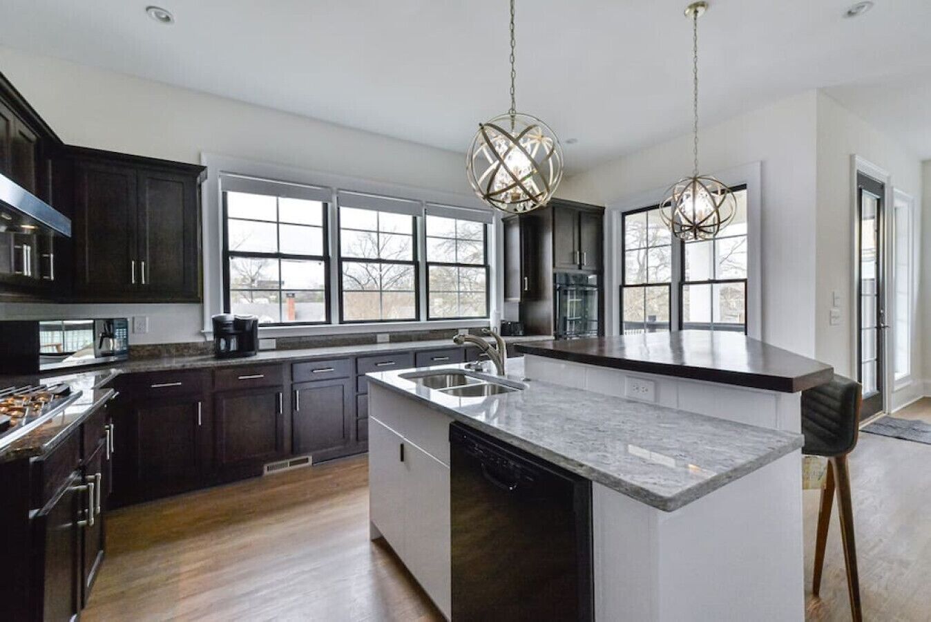 A modern kitchen with dark cabinetry, a large island with a sink, and pendant lighting.