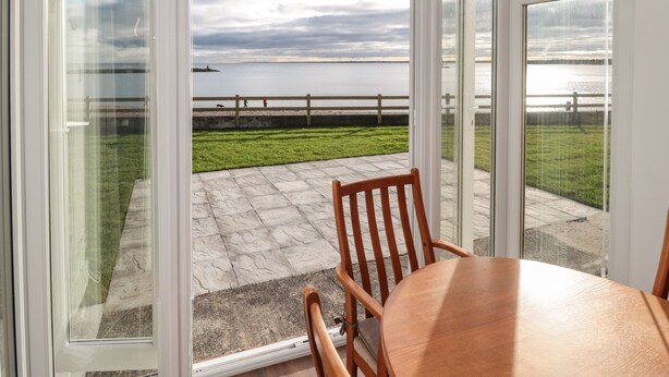 A conservatory with a view of a body of water, a grassy area, and a wooden table and chairs.