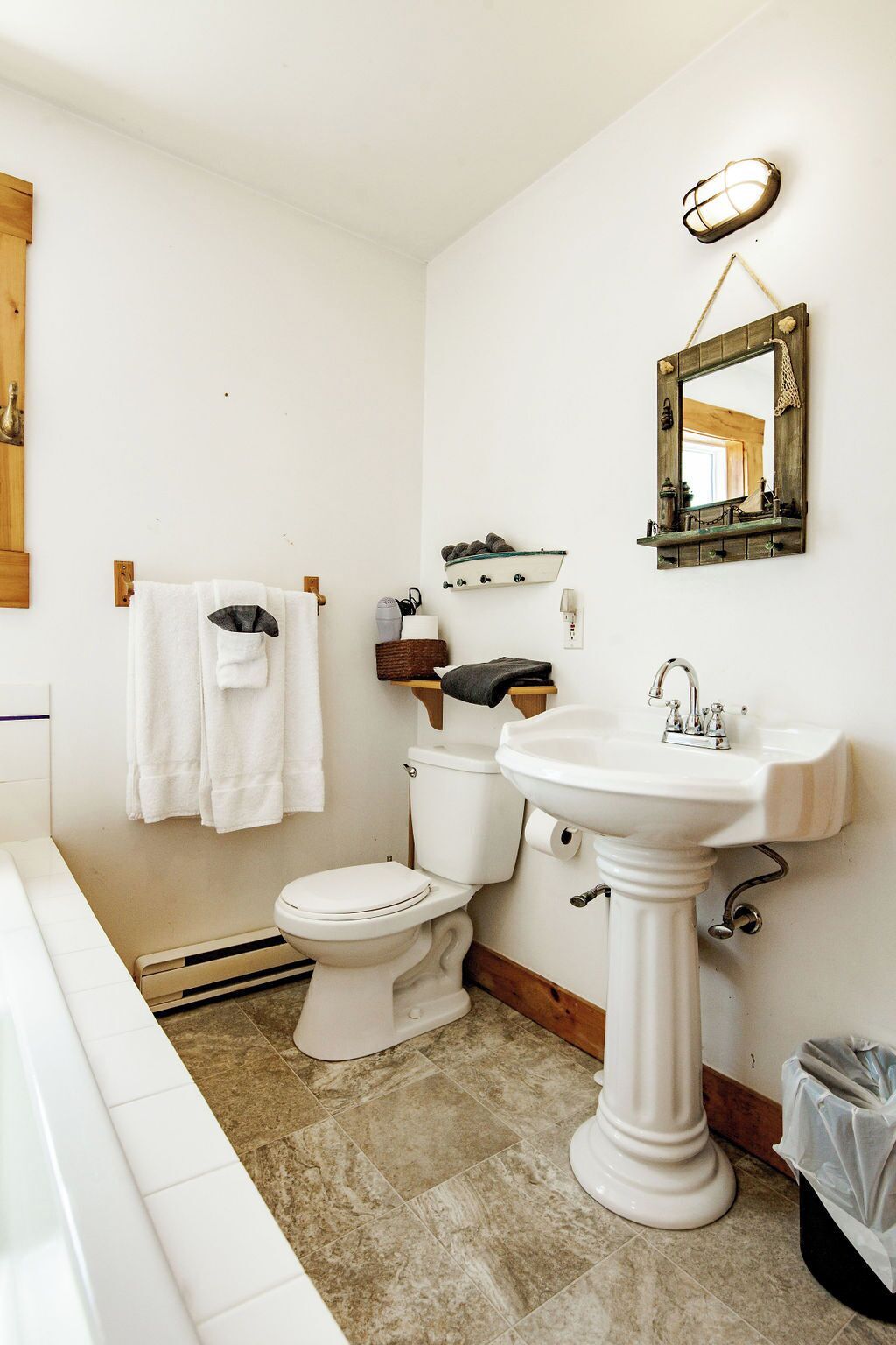 A bathroom with a toilet, sink, and bathtub. There is a towel rack with towels, a mirror, and a shelf with decorative items.