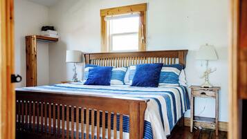 Een slaapkamer met een houten bed, gestreept beddengoed, een nachtkastje met een lamp en een raam boven het bed.