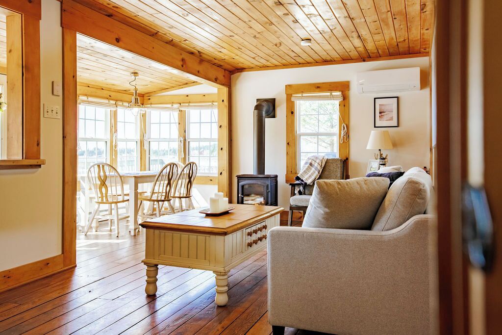 Un salon chaleureux avec un plancher en bois, une cheminée, un coin repas avec des chaises et un canapé.