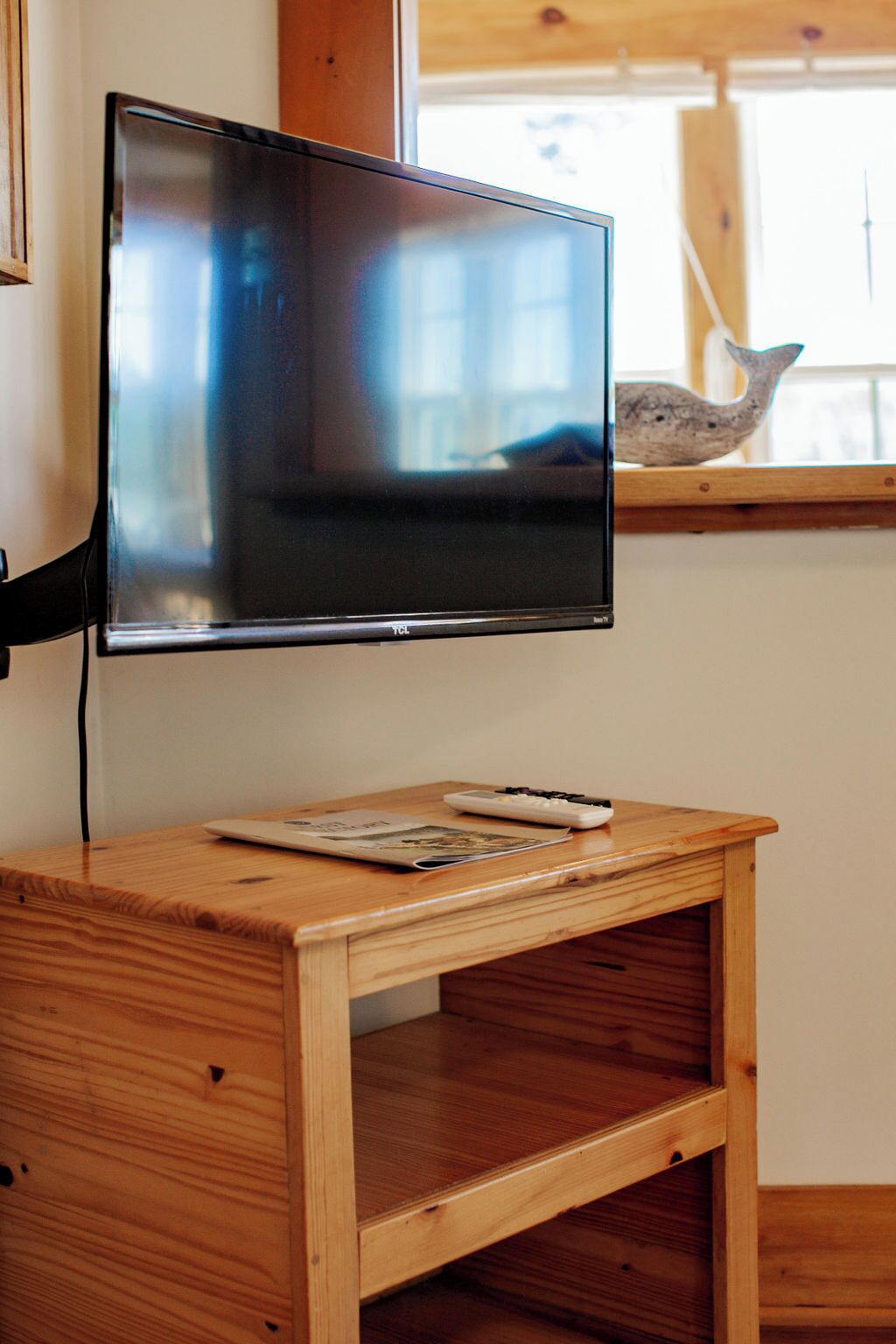 Un televisor de pantalla plana montado en una pared sobre una mesa de madera, con un control remoto y una revista.