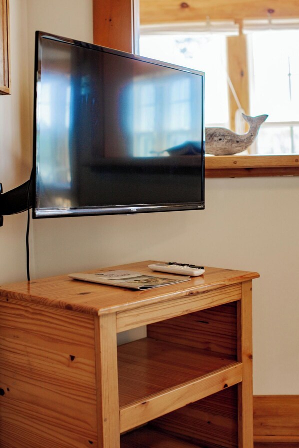 Un televisor de pantalla plana montado en una pared sobre una mesa de madera, con un control remoto y una revista.