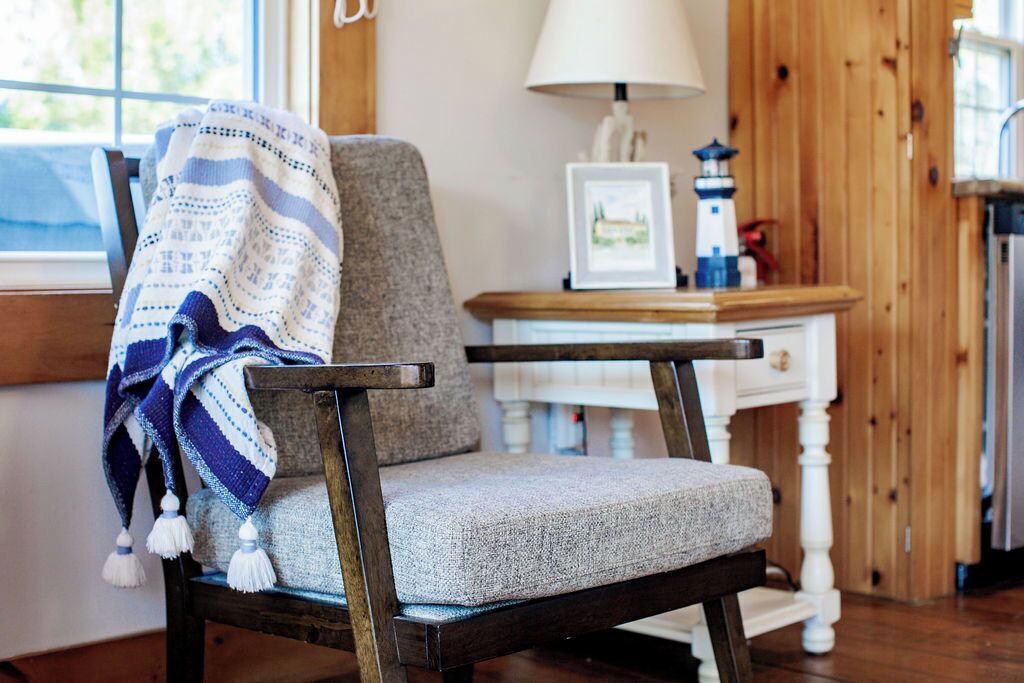 Una habitación acogedora con una silla de madera, una lámpara y un cuadro en una mesa de madera.