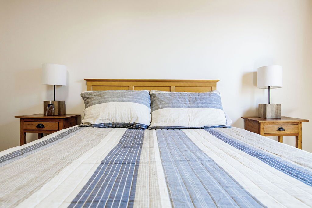A bed with a striped bedspread, two bedside tables with lamps, and a wooden headboard.