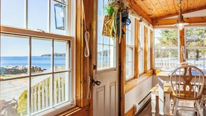 Une pièce dotée de grandes fenêtres donnant sur une plage, avec des murs en bois, une porte blanche et une chaise en bois.
