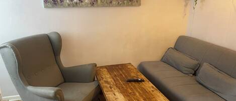 A room with a grey armchair, a grey sofa, and a wooden coffee table with a remote control on it.