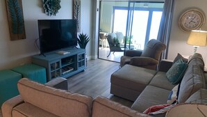 Un salon doté d’un téléviseur à écran plat, d’un meuble de rangement turquoise, d’un canapé marron et d’un coin repas visible à travers une porte vitrée.