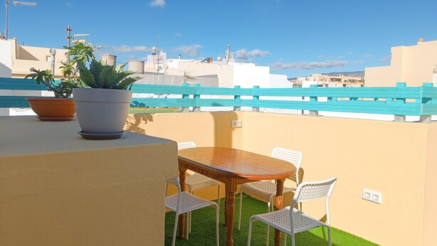 A rooftop terrace with a wooden table and white chairs, surrounded by potted plants. - Daydream El Medano Coliving (Granadilla de Abona)