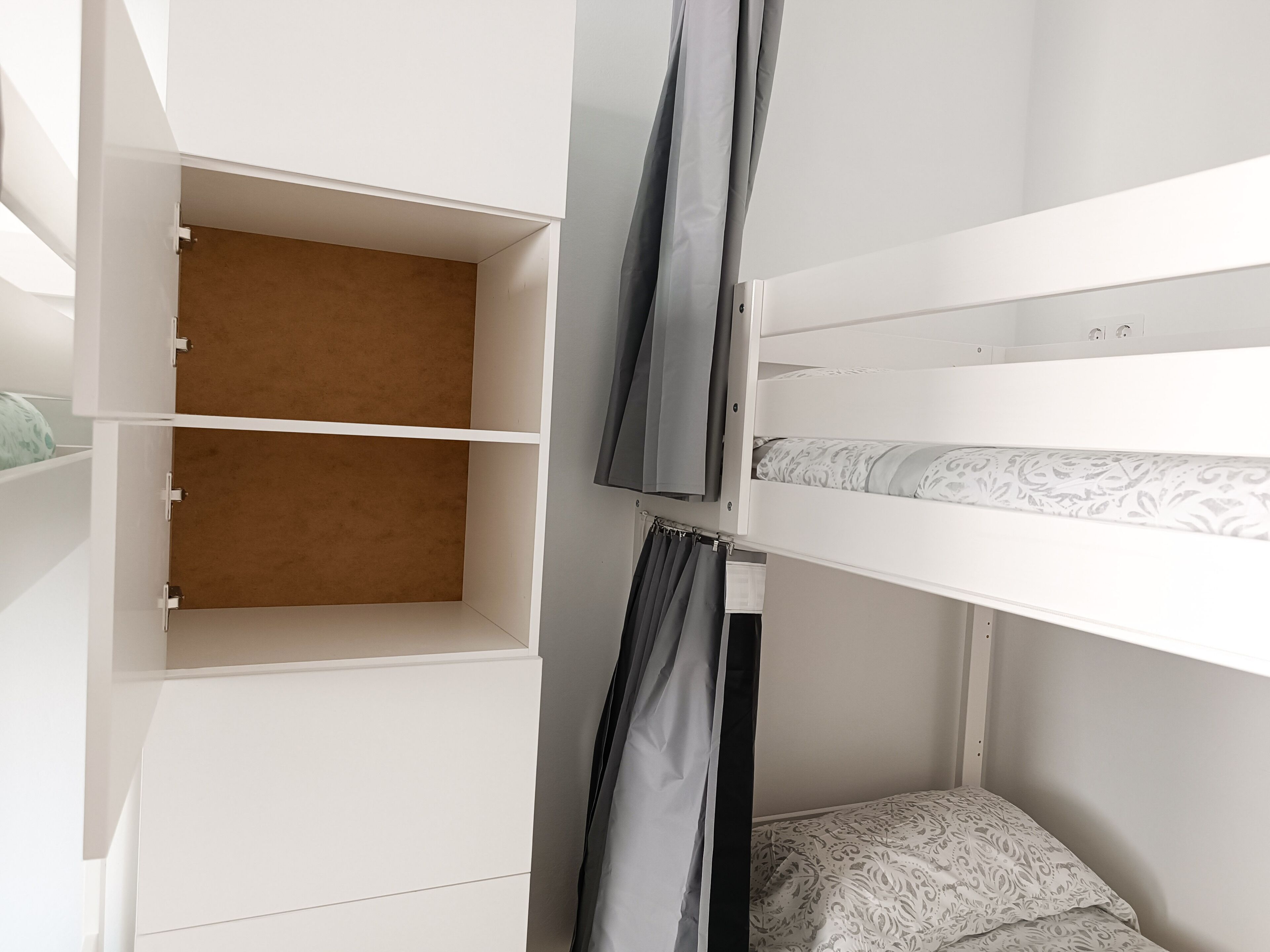 Una cama litera con un espacio de almacenamiento debajo, una cortina y una colcha estampada.