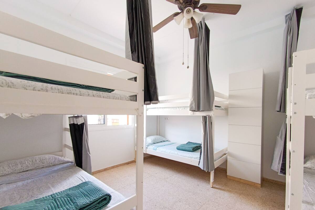 A dormitory room with bunk beds, a ceiling fan, and a window.