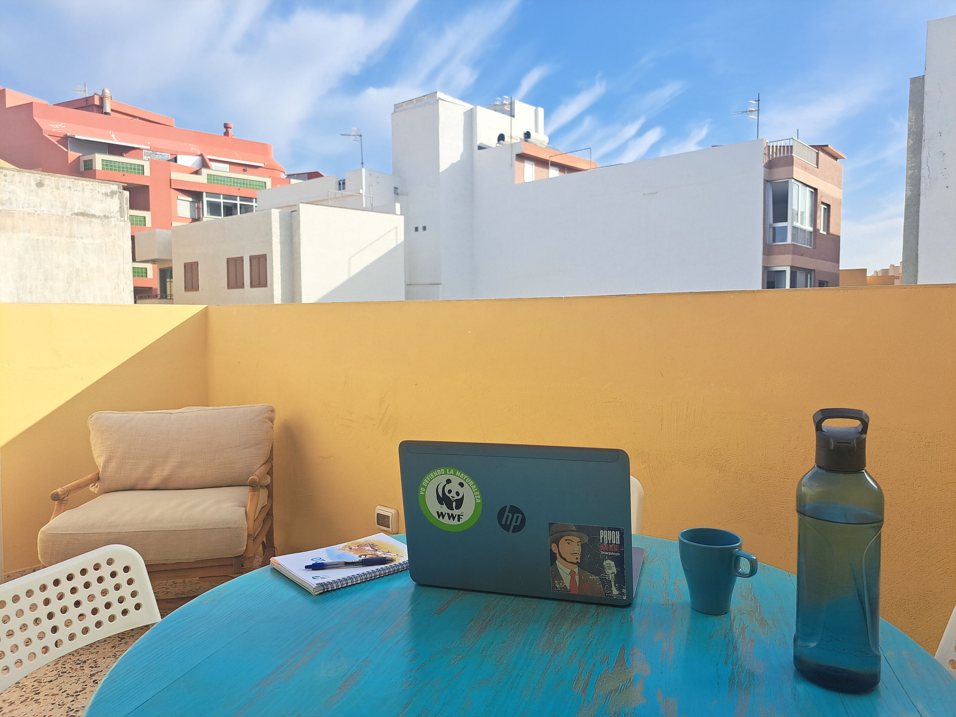 A blue table with a laptop, a notebook, a pen, a mug, and a water bottle.