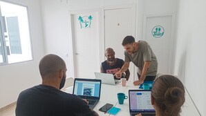 A meeting room with white walls, a white door, and a window. There are three people seated at a table with laptops and a coffee cup. - Daydream El Medano Coliving (Granadilla de Abona)