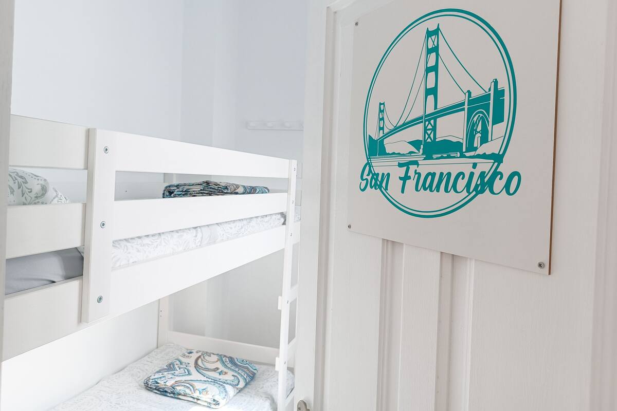A bunk bed with patterned bedding, a wall-mounted San Francisco bridge graphic, and a white door.