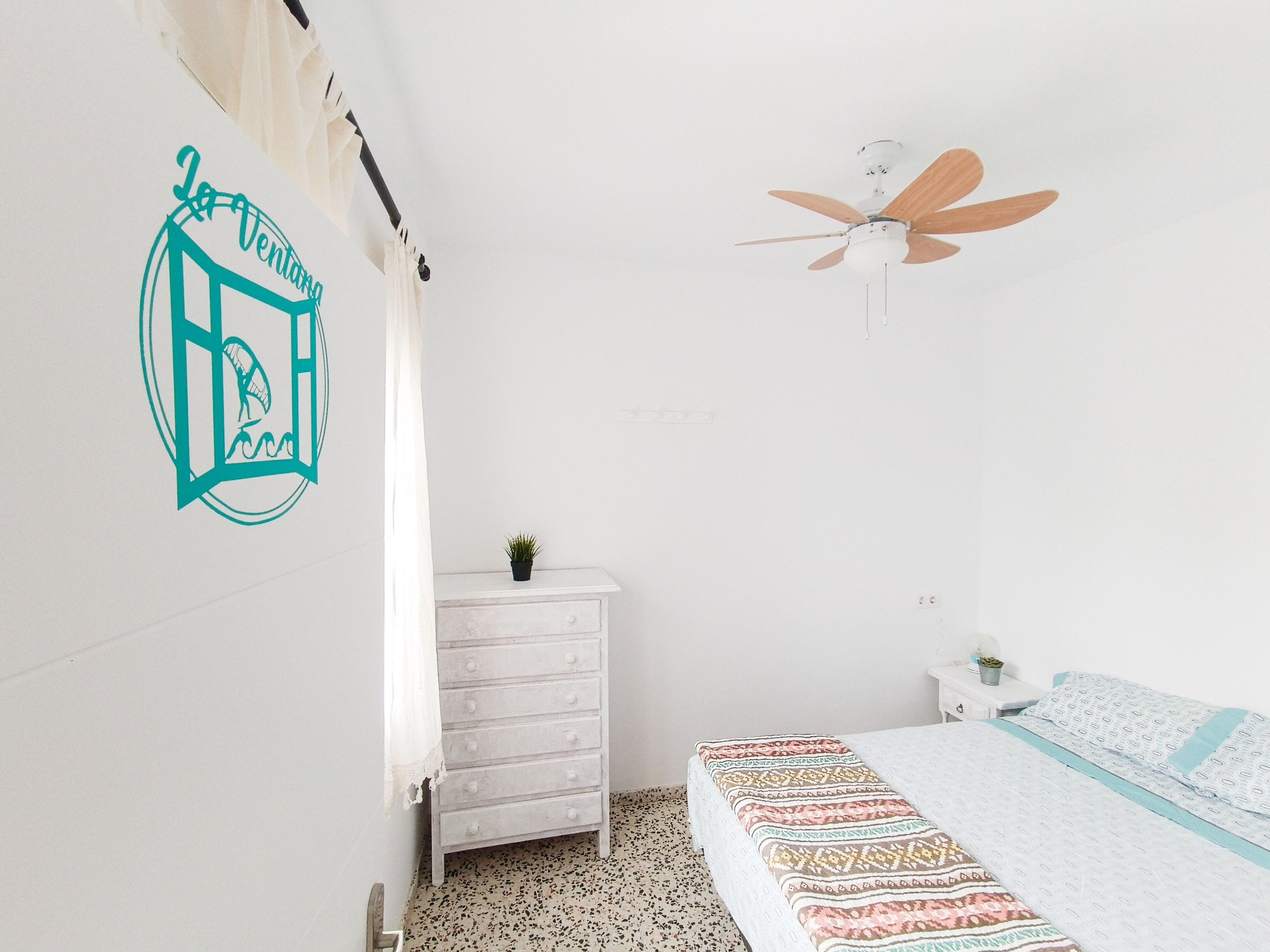 Ein Schlafzimmer mit Bett, Deckenventilator, Kommode und einer kleinen Pflanze.