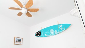 A ceiling fan with wooden blades, a blue surfboard with white designs, and a framed photograph on the wall. - Daydream El Medano Coliving (Granadilla de Abona)