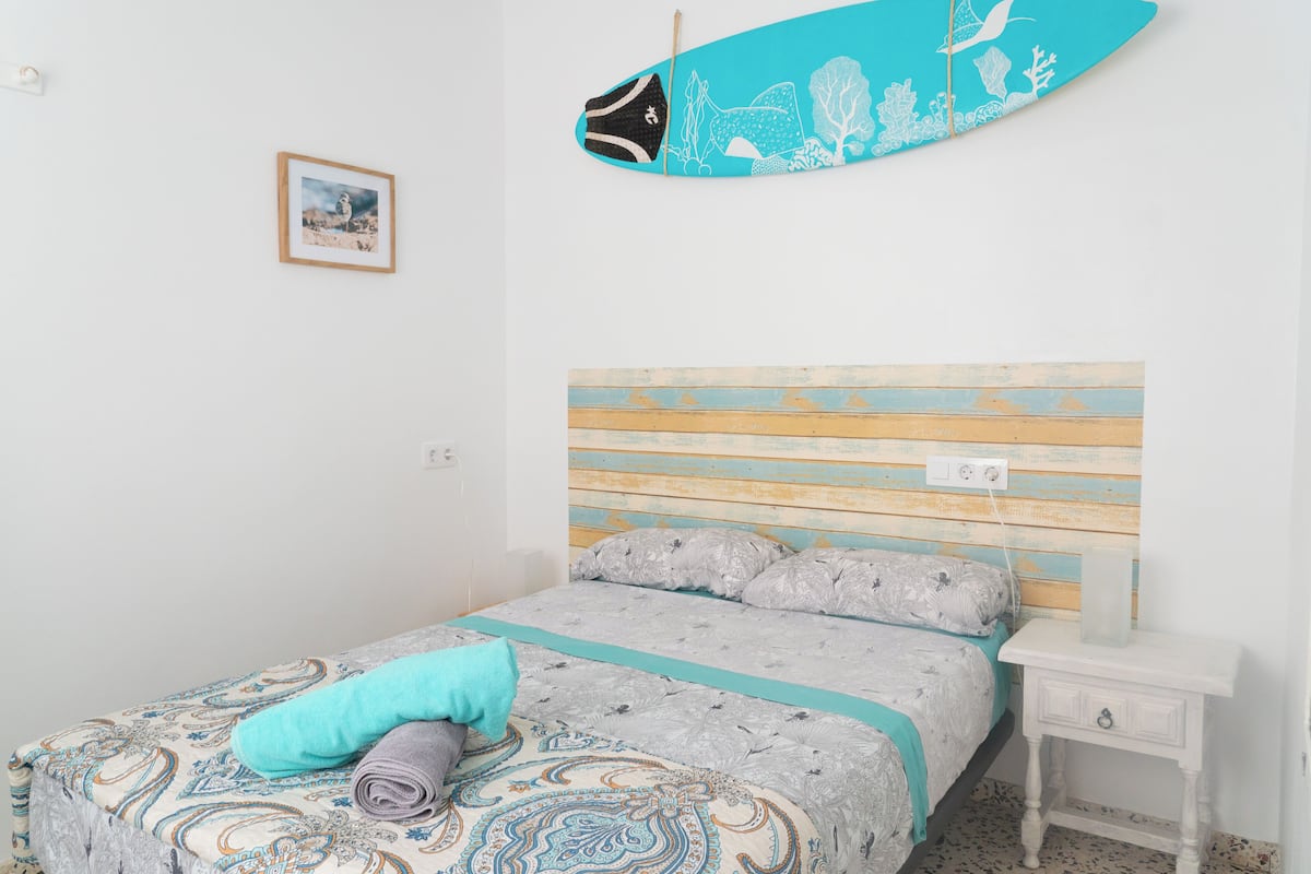 A bedroom with a bed, a nightstand, a surfboard, and a framed picture on the wall.