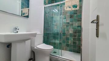 Une salle de bain avec un lavabo blanc, des toilettes et une douche en verre, dont les murs sont recouverts de carreaux verts.