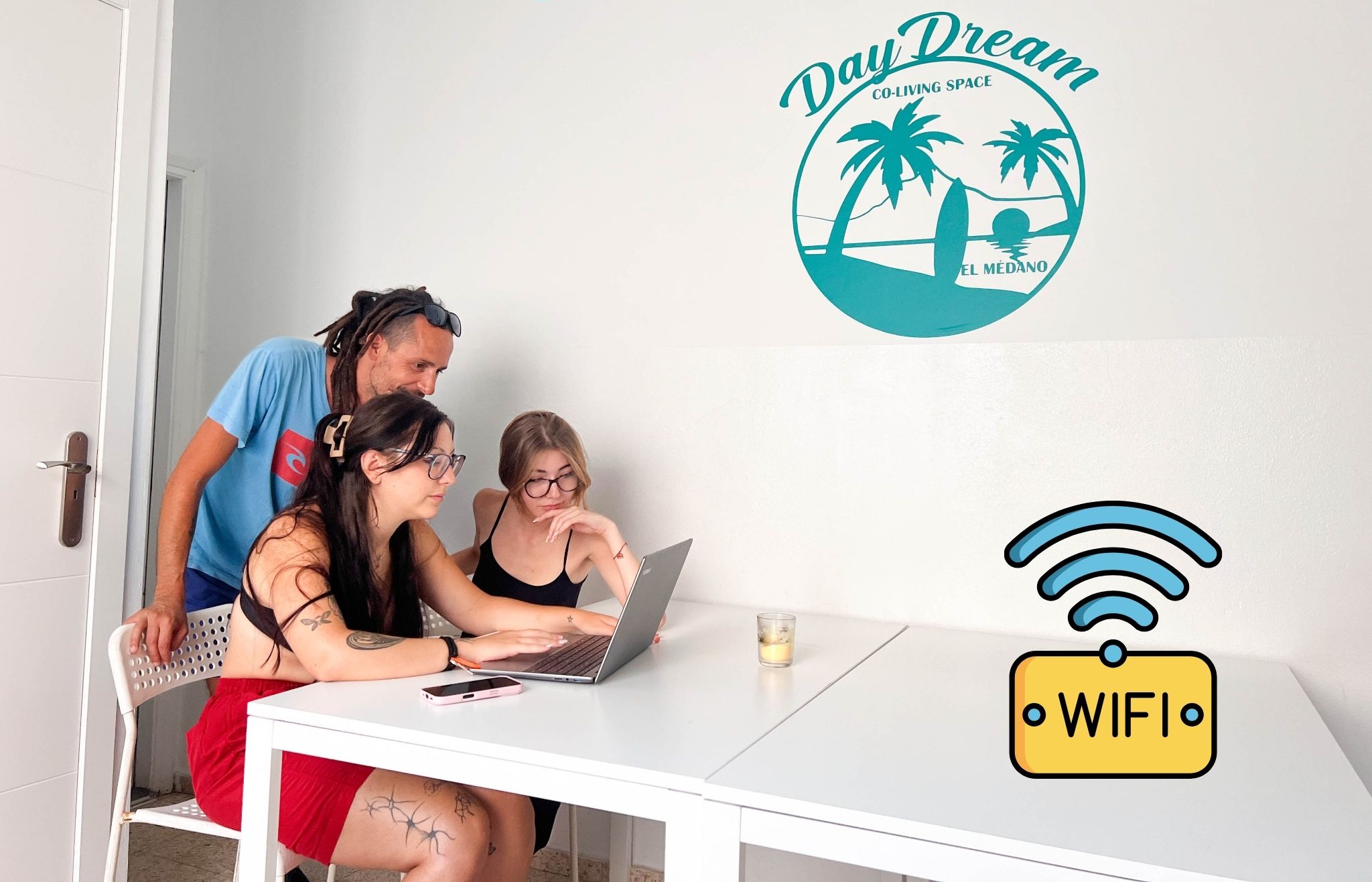 Un espace de travail partagé avec une table blanche, un ordinateur portable et un smartphone. On y voit le logo de « Day Dream Co-Living Space » et un symbole indiquant la présence d’une connexion Wi-Fi.