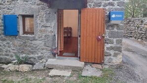 Un edificio de piedra con techo de tejas, una puerta de madera y una ventana pequeña con persiana azul.