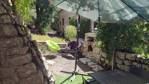 Un patio con pared de piedra, una silla verde, una mesa y una pérgola que da sombra.