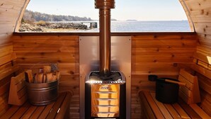 A wooden sauna with a glass ceiling, a visible fire, and a bench on the left. - Romantic Oceanfront Studio | Private Hot Tub | Fireplace | Near Halifax (Boutiliers Point)