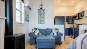 A cozy living room with a sofa, ottoman, and a black wood-burning stove.