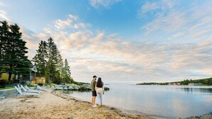 A beach with lounge chairs, a wooden deck, and a calm lake.