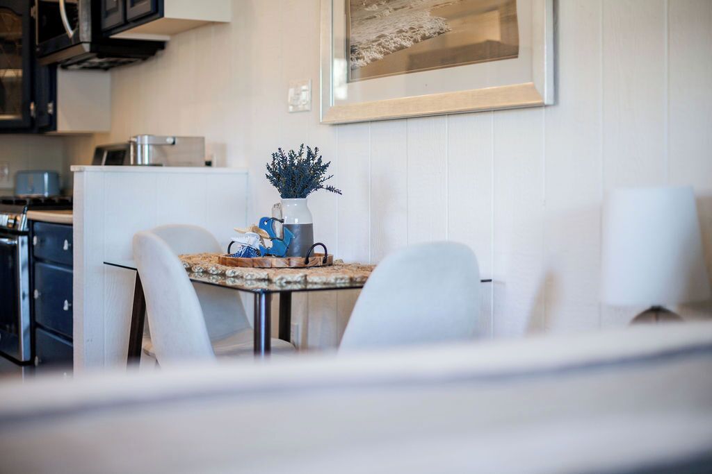 Une cuisine moderne avec des meubles blancs, une table à manger avec des chaises et un vase rempli de fleurs bleues posé sur la table.