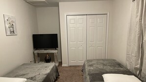 Een slaapkamer met twee enkele bedden, een televisie op een klein tafeltje en een witte deur.