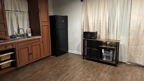 Een keuken met houten kastjes, een zwarte koelkast, een magnetron op een houten plank en een wastafel met een kraan.