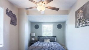 Une chambre à coucher avec un lit, un ventilateur de plafond, une fenêtre et des éléments de décoration murale.