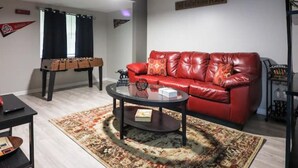 Un salon avec un canapé en cuir rouge, une table basse, une table de baby-foot et un tapis.