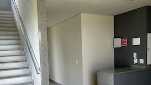 A modern interior with a staircase, a reception desk, and a plain wall with a fire alarm. - Hotel Penedo Inn (Itatiaia)