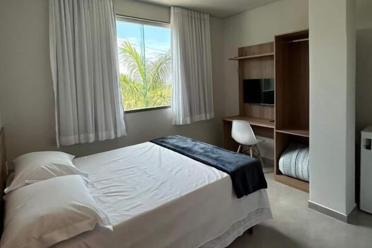 A bedroom with a bed, a desk, a chair, a TV, and a wardrobe.