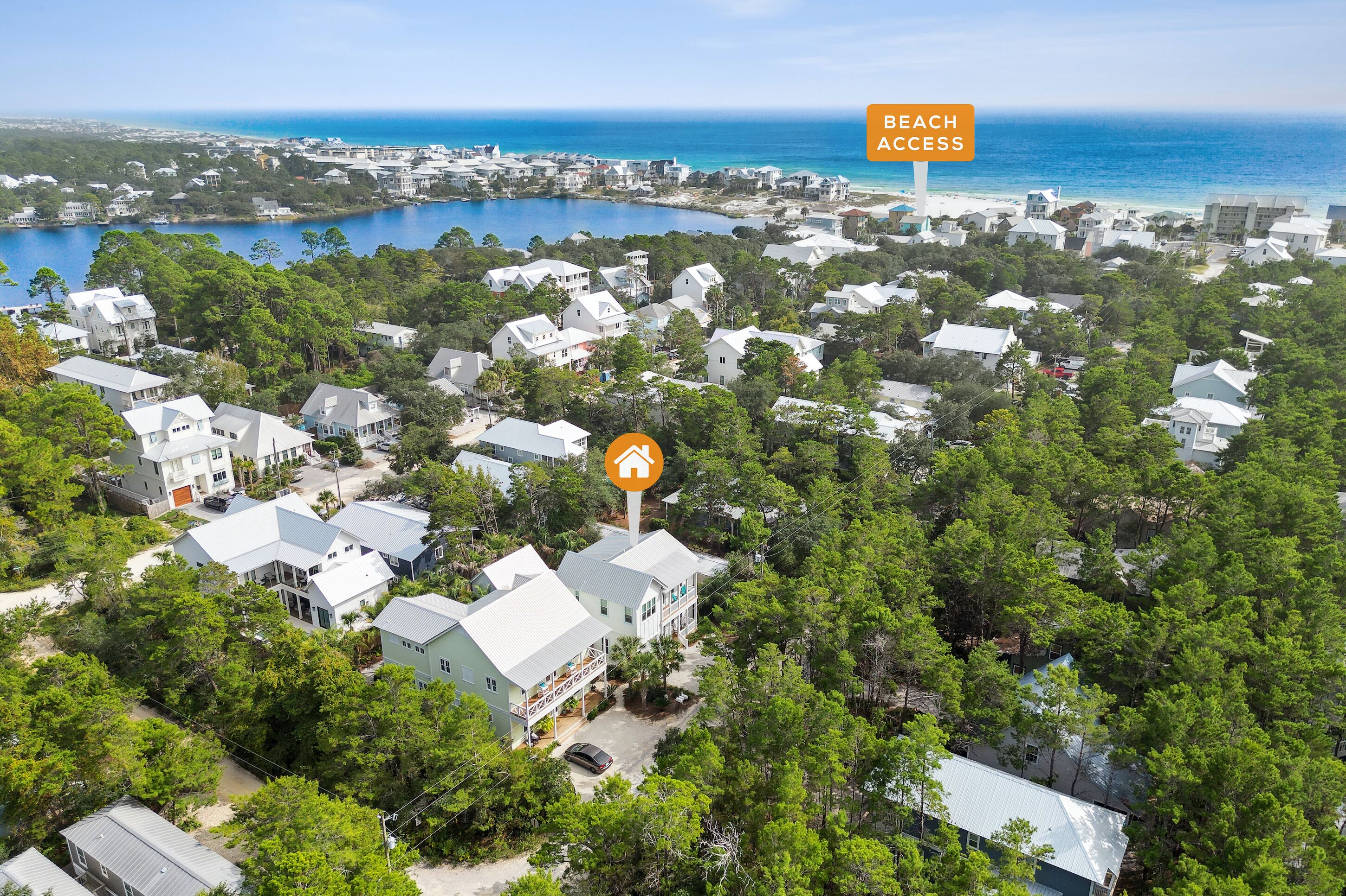 A residential area with houses surrounded by trees and a beach access sign.