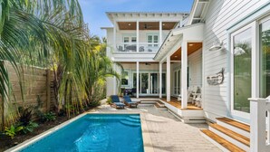 Una casa de dos pisos con piscina, zona de estar exterior y un porche cubierto.