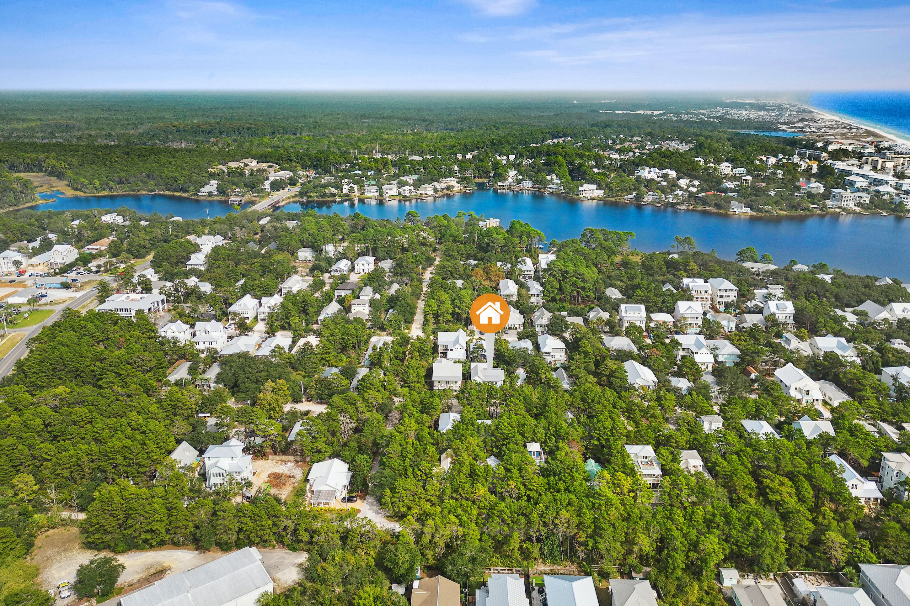 An aerial view of a residential area with houses surrounded by dense trees and a large body of water.