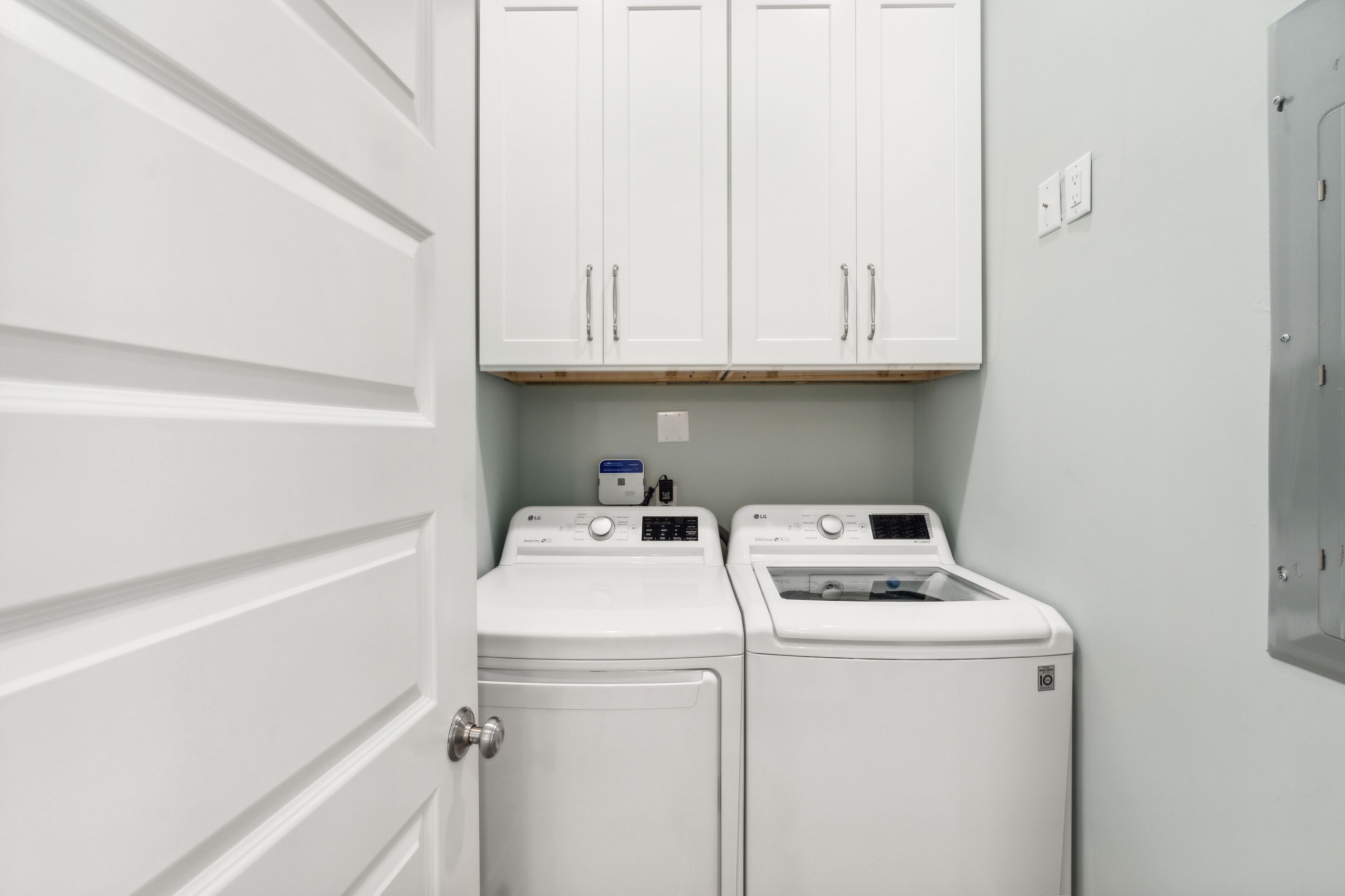 A laundry room with two front-loading washing machines, a white door, and a white cabinet above the machines.