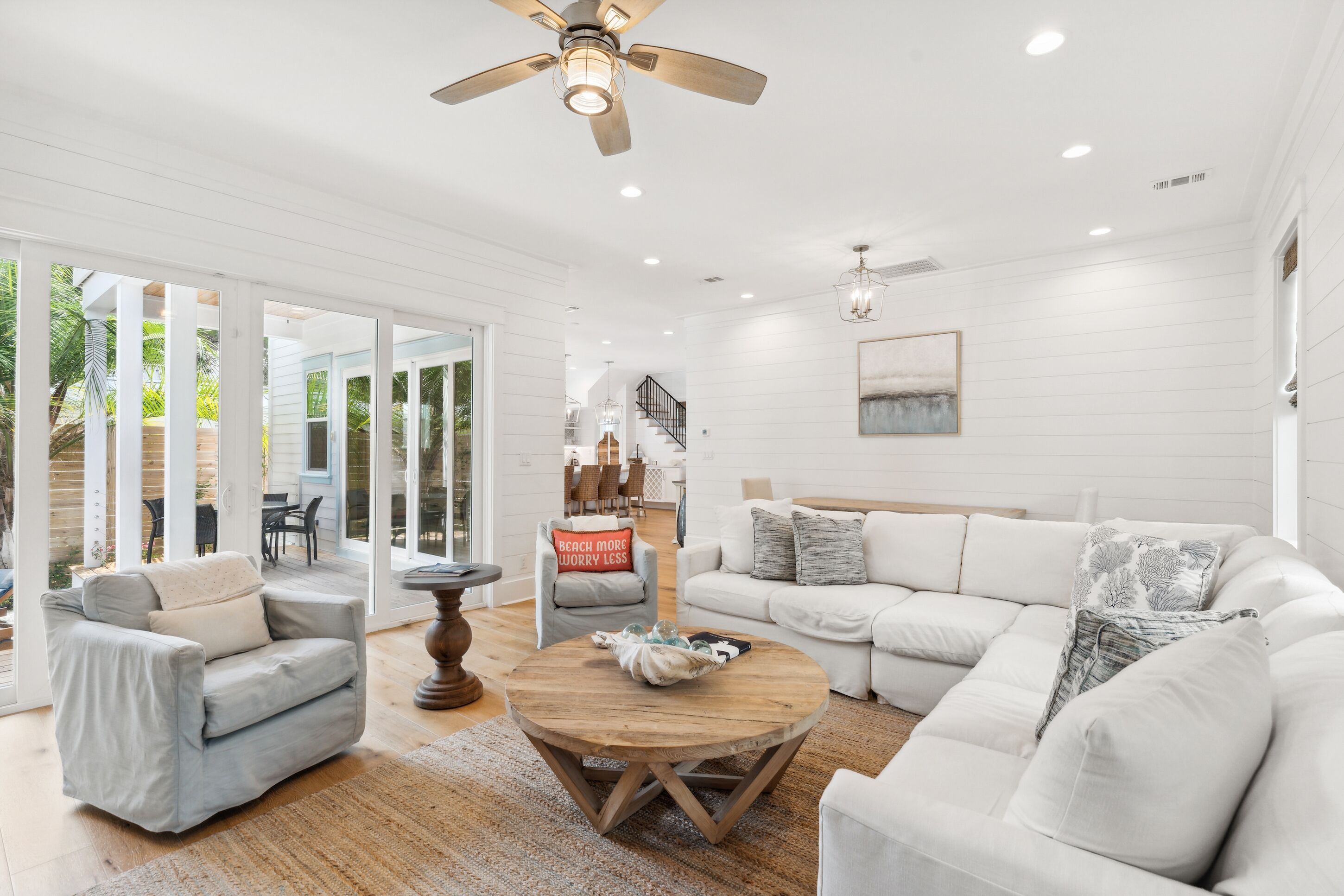 A spacious living room with a white color scheme, featuring a large sofa, a coffee table, and a ceiling fan.
