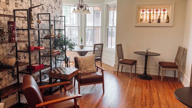 A cozy living room with a wooden floor, a bookshelf, a chessboard, and a dining area with chairs and a table.