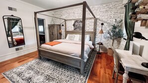 A four-poster bed with a wooden frame, a patterned rug, and a stone wall backdrop.