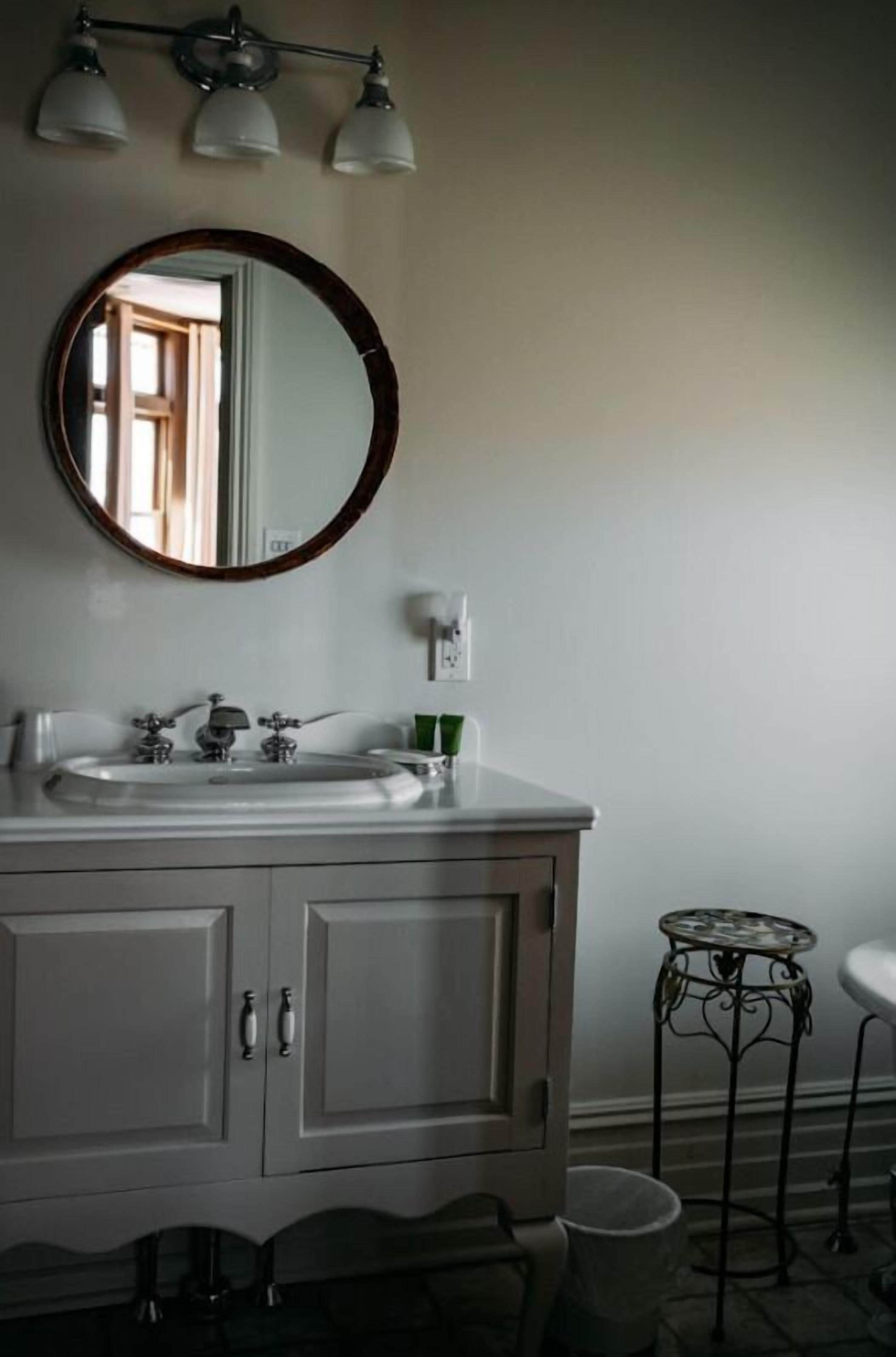 A bathroom with a white vanity, a round mirror, and a small round table.
