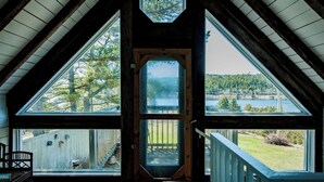 A cabin with a large bay window, a hexagonal skylight, and a view of a lake and forest.
