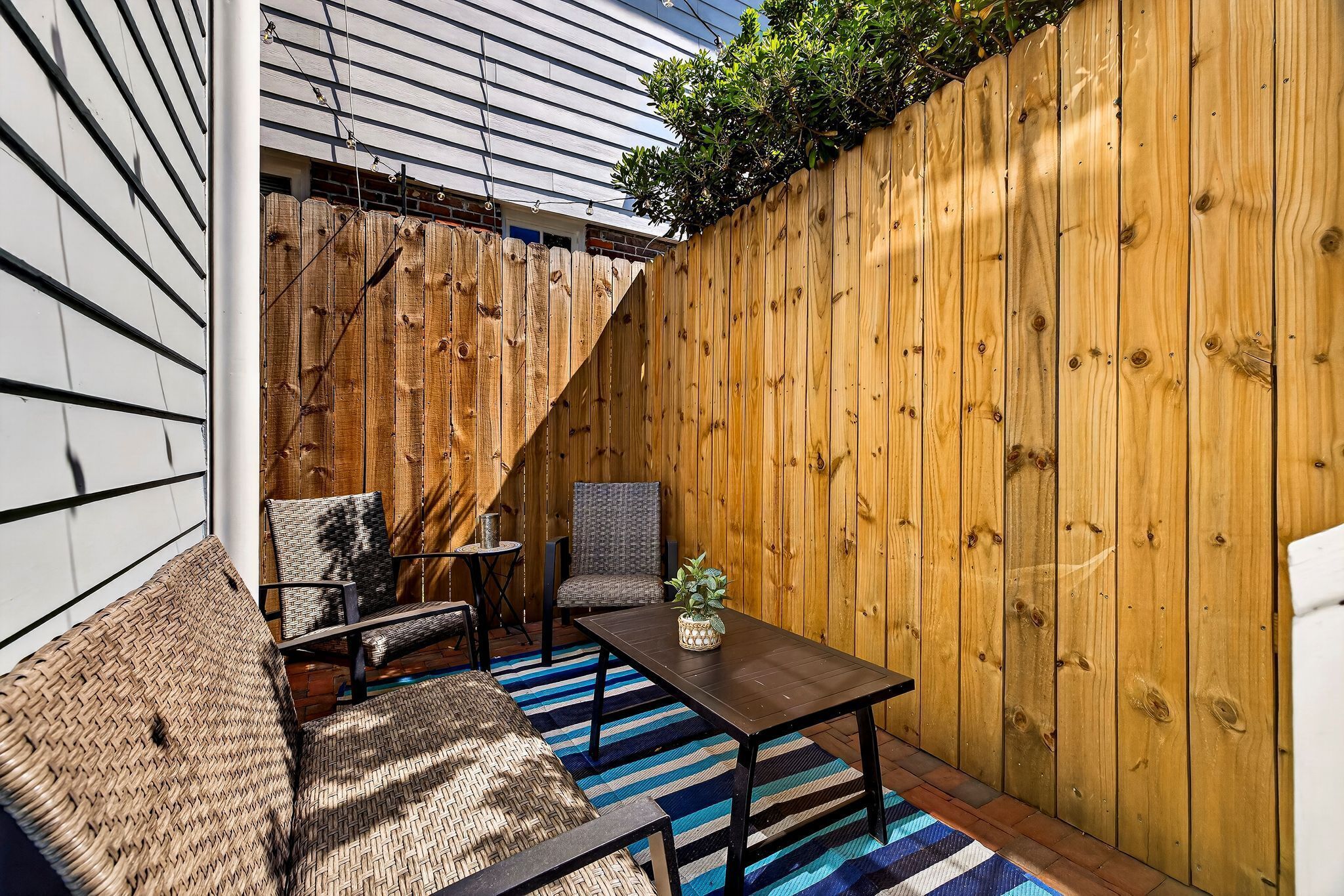 Un patio con cerco de madera, una mesa, dos sillas y una planta pequeña.