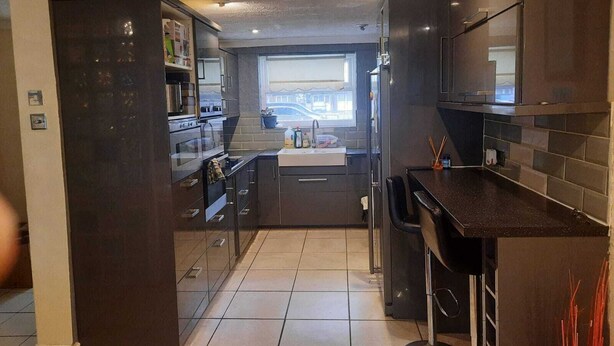 A modern kitchen with dark cabinetry, a central island, and a window providing a view of the outside. - Remarkable 3-bed House in London (London)