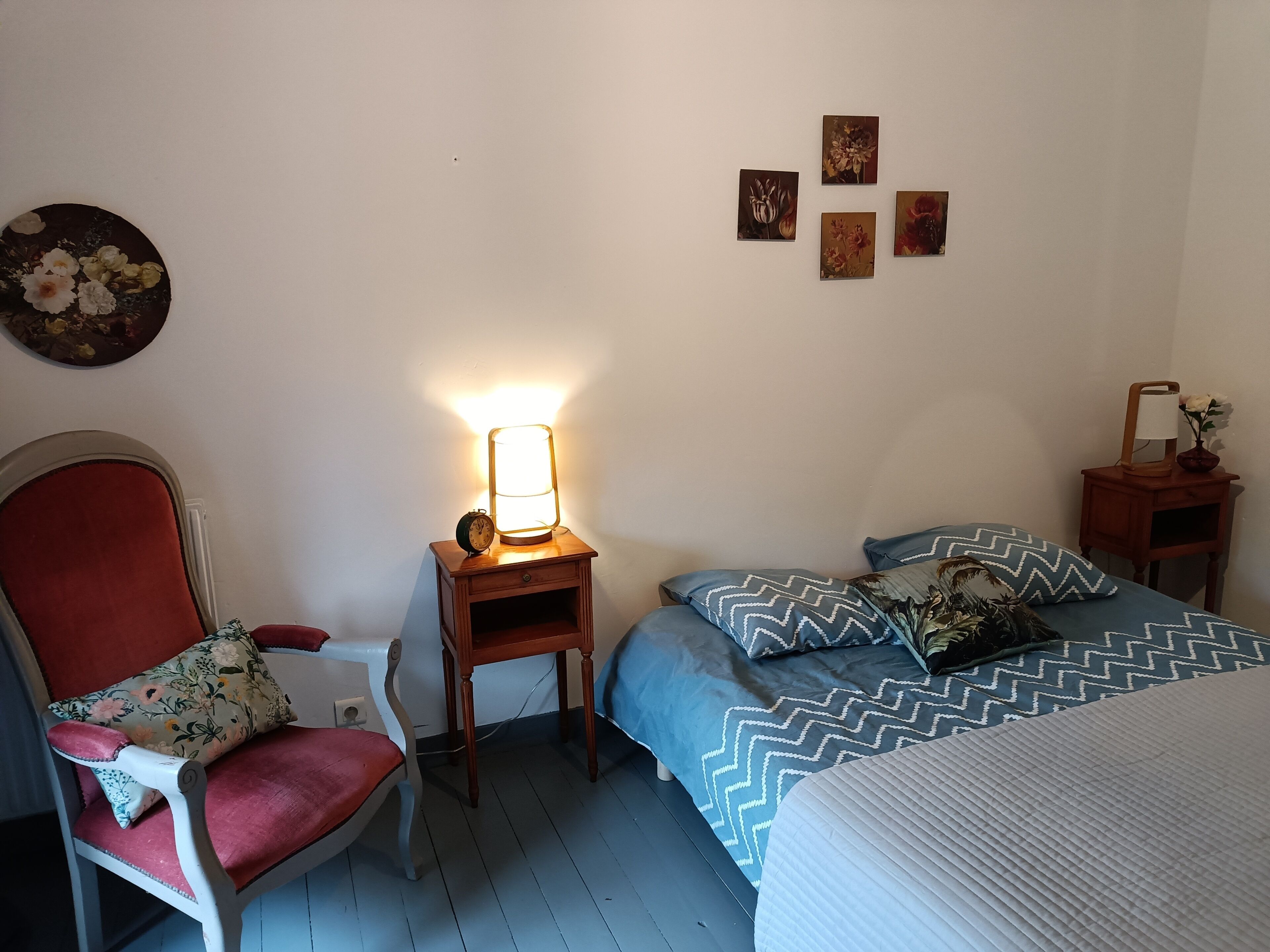 Une chambre avec un lit simple, une chaise, une table de chevet avec une lampe et une horloge murale.