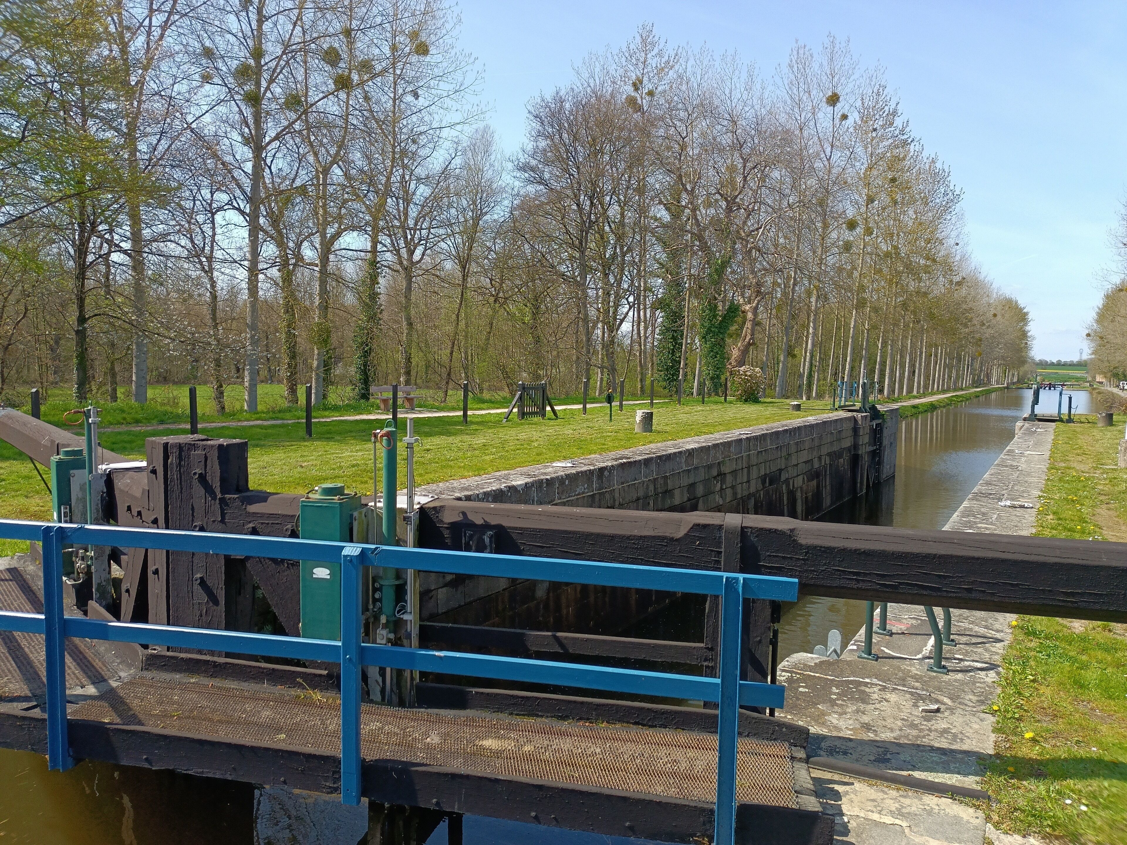 Un canal doté d’un système d’écluses, une zone herbeuse avec des arbres et un sentier.