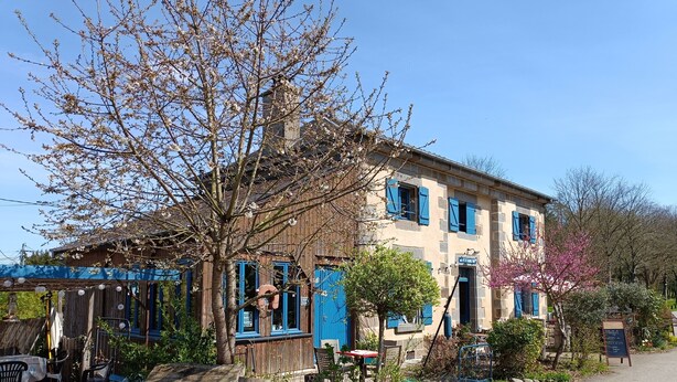 A rustic building with blue shutters, a wooden porch, and a garden area with a bench. - Maison Éclusière Napoléonienne, Havre de Paix au Bord du Canal D'ille et Rance (Hédé-Bazouges, Hédé)