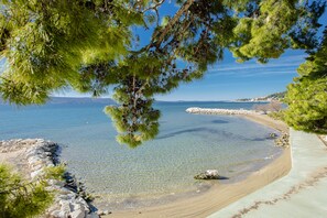Una vista despejada al mar con una playa arenosa, costa rocosa y árboles verdes y frondosos.